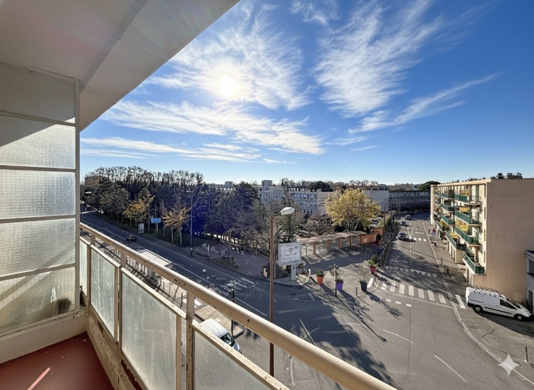 Cette photo montre la vue dégagée depuis le balcon d'un appartement situé à Avignon. On y voit un paysage urbain avec des arbres et des bâtiments sous un ciel ensoleillé