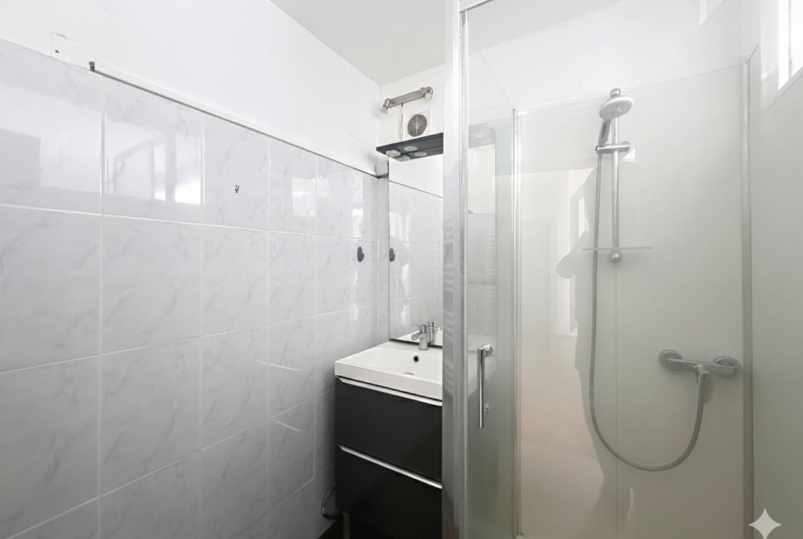 Cette image présente la salle d'eau rénovée de l'appartement à Avignon. Elle comprend un lavabo avec un meuble sous vasque et une cabine de douche vitrée.