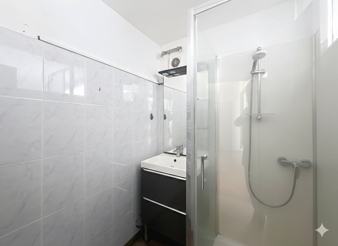 Cette image présente la salle d'eau rénovée de l'appartement à Avignon. Elle comprend un lavabo avec un meuble sous vasque et une cabine de douche vitrée.