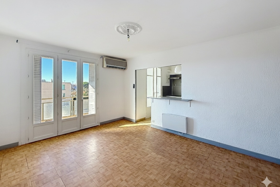 Vue d'ensemble du séjour avec aperçu de la cuisine de l'appartement T3 à Avignon. Le sol est en parquet et les pièces sont baignées de lumière naturelle.