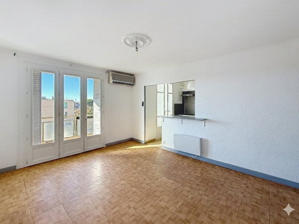 Vue d'ensemble du séjour avec aperçu de la cuisine de l'appartement T3 à Avignon. Le sol est en parquet et les pièces sont baignées de lumière naturelle.