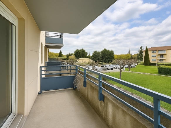Terrasse avec garde-corps bleus offrant une vue sur les jardins et le parking résidentiel. L’espace est accessible depuis la pièce de vie par une baie vitrée