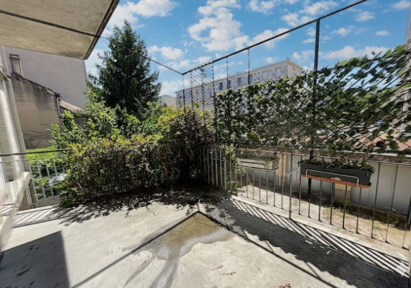errasse bétonnée avec garde-corps métallique et végétation en fond. L’espace extérieur bénéficie d’un bon ensoleillement et d’une vue dégagée sur la cour de la résidence.