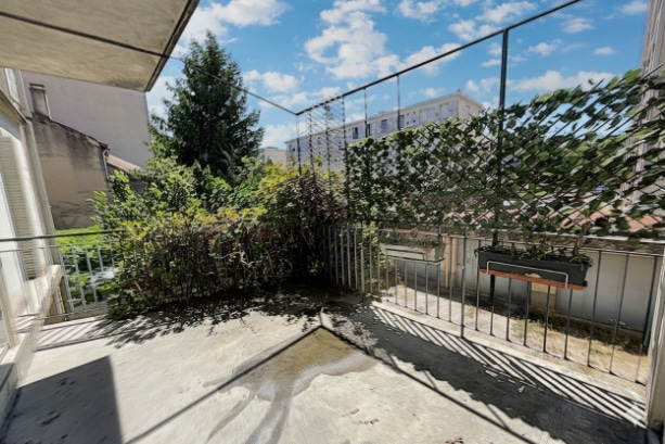 errasse bétonnée avec garde-corps métallique et végétation en fond. L’espace extérieur bénéficie d’un bon ensoleillement et d’une vue dégagée sur la cour de la résidence.