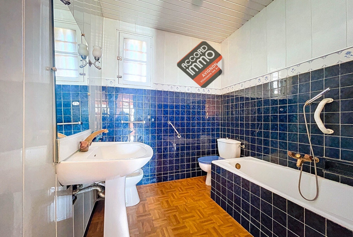 Salle de bain lumineuse et moderne avec carrelage bleu et sol en parquet, équipée d'une baignoire, d'un lavabo et de toilettes située dans une maison avec jardin à vendre à Avignon