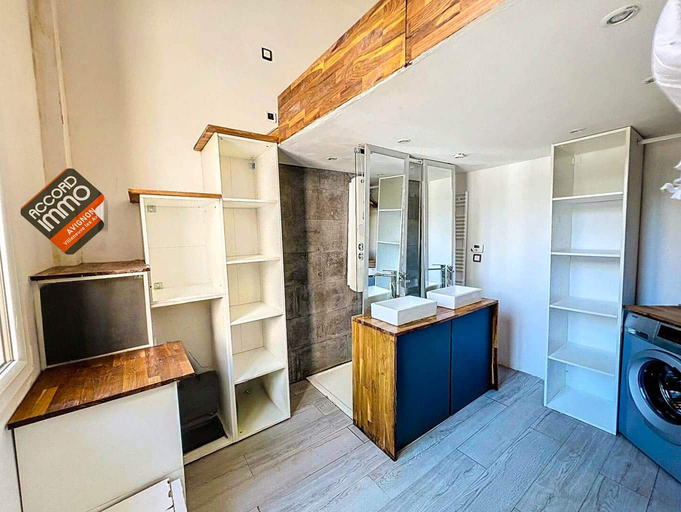 Vue d'une salle de bain avec double vasque, meubles en bois, douche moderne et rangements intégrés, située dans une maison T2 à Avignon proche des remparts.