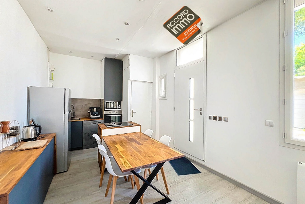 Cuisine avec meubles en bois, réfrigérateur, plaques de cuisson et espace repas dans une maison T2 située près des remparts d'Avignon.