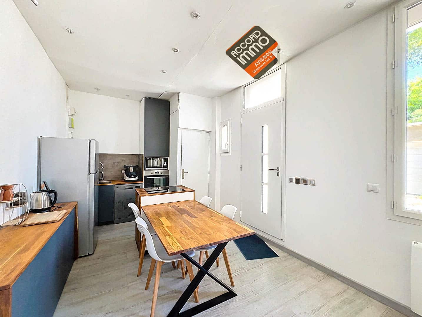 Cuisine avec meubles en bois, réfrigérateur, plaques de cuisson et espace repas dans une maison T2 située près des remparts d'Avignon.
