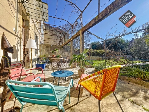 Terrasse extérieure ensoleillée d’une maison à vendre à Avignon, avec mobilier coloré et vue sur le jardin arboré