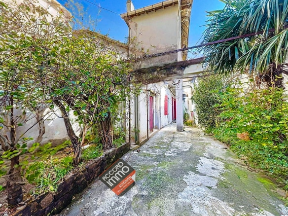 Cour pavée entourée de végétation donnant accès à un immeuble de rapport situé à Avignon. Bien immobilier proposé à la vente pour un investissement locatif