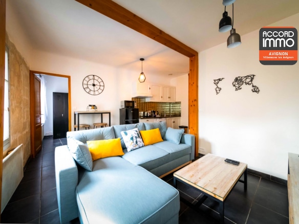 Vue du salon moderne avec canapé et cuisine ouverte dans un appartement T2 meublé à vendre en centre historique d’Avignon