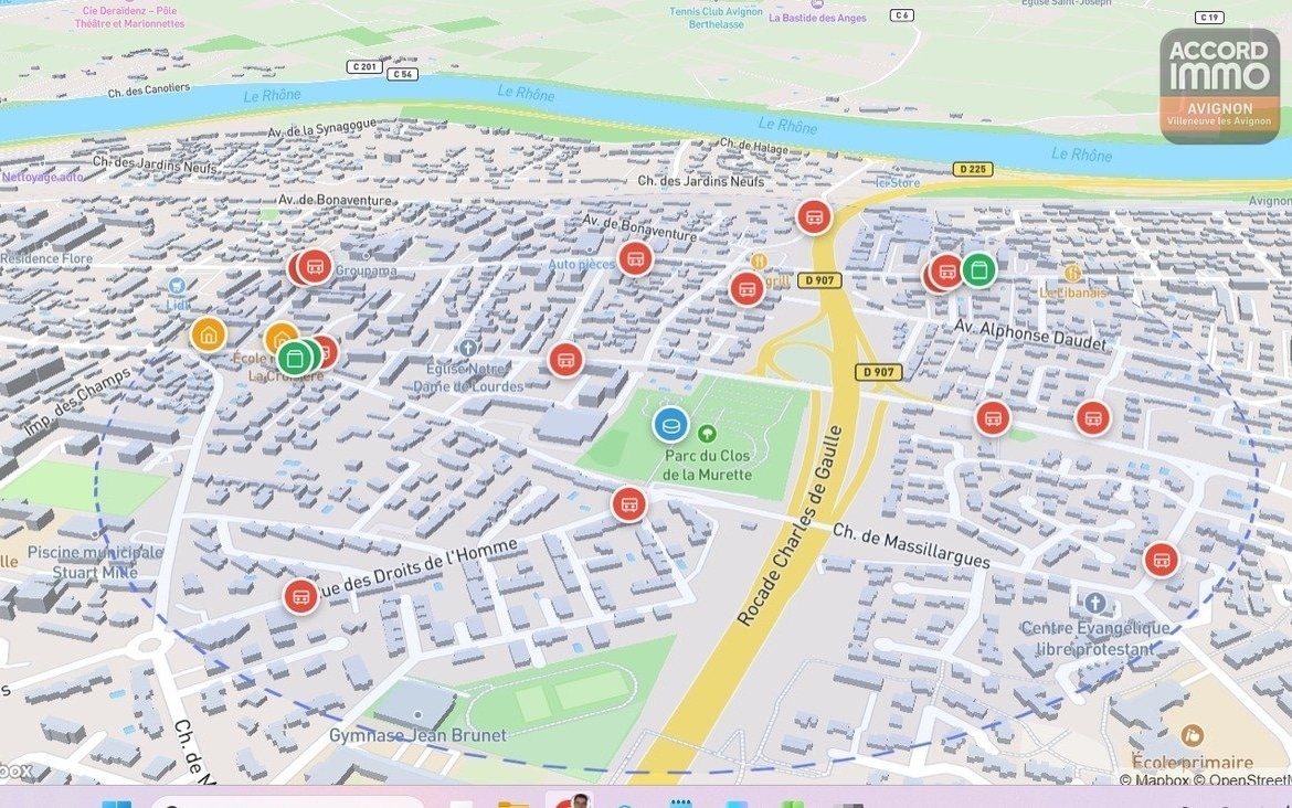 Vue cartographique en 3D du quartier de Villeneuve-lès-Avignon montrant les rues, le Rhône et les commerces environnants. Points d'intérêt indiqués incluant écoles, parcs et axes routiers principaux.
