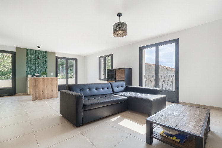 Grand salon lumineux avec canapé d’angle et baies vitrées dans une maison contemporaine à Vacqueyras