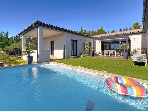 Espace extérieur comprenant une piscine et une terrasse aménagée devant les baies vitrées. Le jardin est arboré et entouré de haies avec une belle luminosité