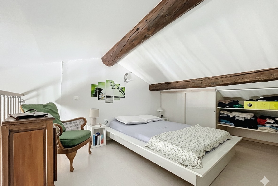 Chambre aménagée sous les toits avec poutres en bois apparentes, mobilier moderne et dressings intégrés. Espace nuit lumineux au dernier étage d'un appartement dans hôtel particulier à Avignon.