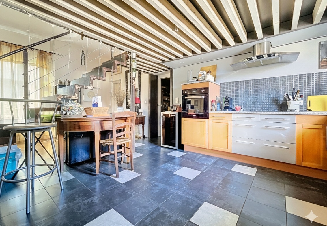 Cuisine aménagée ouverte sur espace repas avec poutres peintes au plafond et carrelage damier au sol. Accès cellier visible avec table ancienne et rangements intégrés dans appartement centre Avignon.