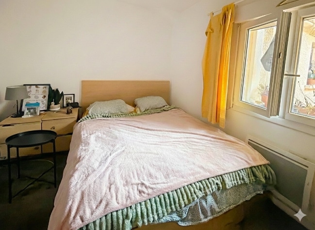 a chambre dispose d’un lit double, de tables de chevet et d’une fenêtre apportant de la lumière naturelle. Les murs sont clairs et le mobilier est disposé de façon fonctionnelle.