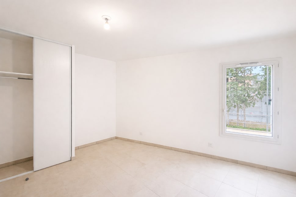 Chambre avec placard coulissant intégré et fenêtre PVC donnant sur l'extérieur avec carrelage beige. Appartement T2 neuf de 46 m² en location à Montfavet dans résidence sécurisée 2025