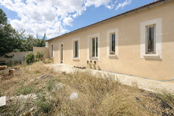 Façade d'une maison indépendante de plain-pied de 55 m² avec enduit beige et fenêtres en PVC double vitrage donnant sur un terrain de 192 m². Construction de 1950 à rénover