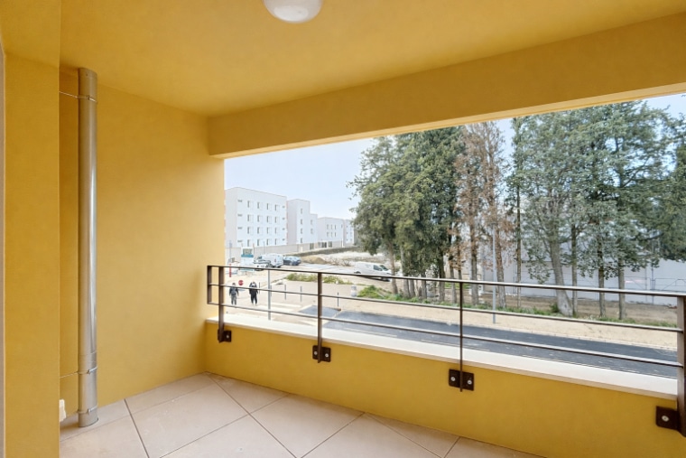 Loggia couverte de 5 m² avec carrelage beige, garde-corps métallique et vue sur espaces verts. Appartement T2 en location à Montfavet dans résidence neuve 2025 avec chauffage collectif électrique inclus.