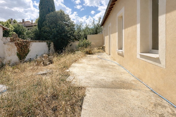 Terrasse extérieure donnant sur un jardin clos de 192 m² entouré d'un mur en parpaing avec végétation existante.