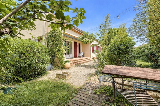 Terrain clos de 749 m² avec végétation dense, arbres fruitiers et espace repas extérieur. Clôture en bois et accès direct depuis la terrasse couverte.