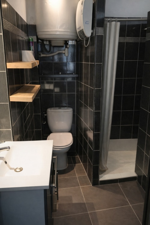 Salle d'eau carrelée gris anthracite avec meuble vasque blanc, WC suspendu et douche à l'italienne. Chauffe-eau électrique mural visible dans cette pièce d'eau d'un immeuble à Avignon.