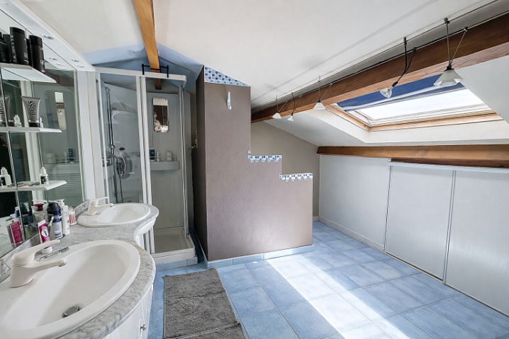 Salle d'eau de 6 m² située à l'étage sous combles aménagés avec fenêtre de toit. Double vasque en marbre, cabine de douche et rangements sous pente.