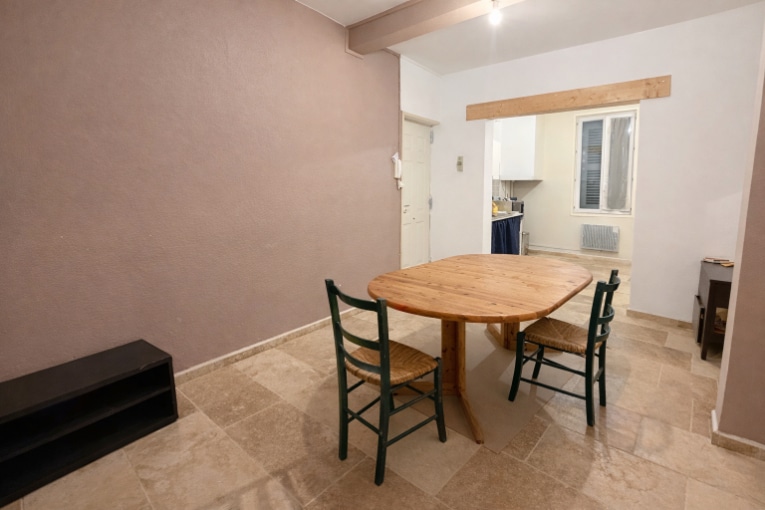 Séjour spacieux avec table ronde en bois massif et vue sur la cuisine semi-ouverte. Le mur rose apporte une touche de couleur à cet espace de vie fonctionnel.