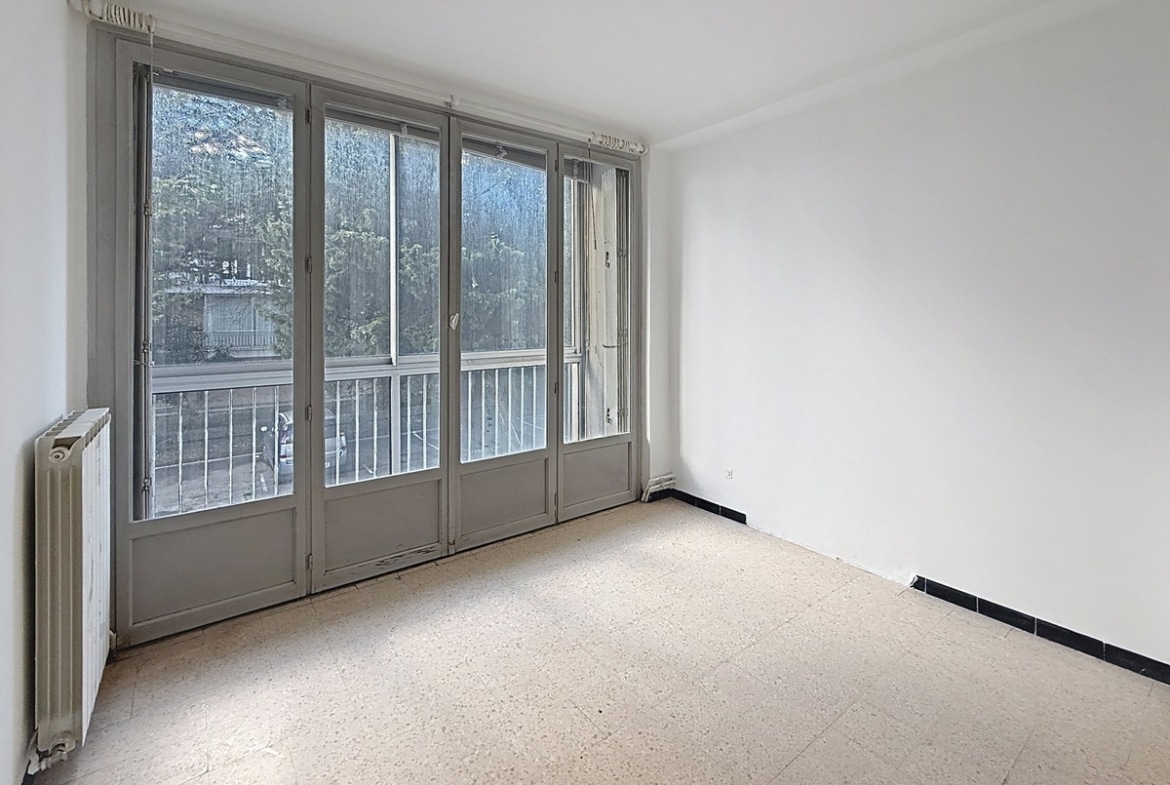 Chambre à coucher avec fenêtre donnant sur l'extérieur, murs clairs et espace pour lit double. Pièce de nuit fonctionnelle au sein d'une résidence avec ascenseur.