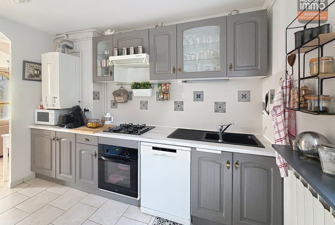 Cuisine fermée avec meubles bas et hauts en bois, plan de travail stratifié et évier sous fenêtre. Électroménager encastré comprenant plaques de cuisson et hotte aspirante murale.