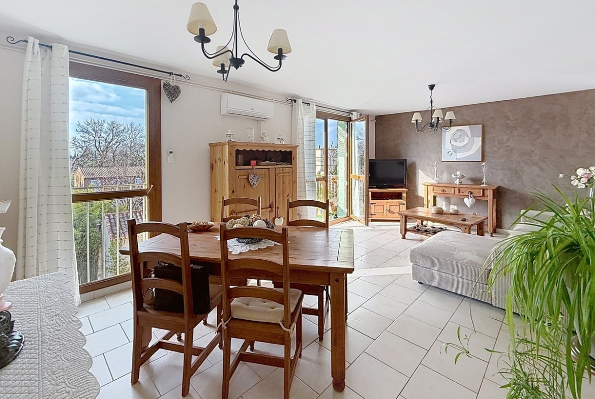 Séjour rectangulaire avec parquet au sol et murs blancs. Baie vitrée coulissante ouvrant sur un balcon avec garde-corps métallique, stores vénitiens aux fenêtres.