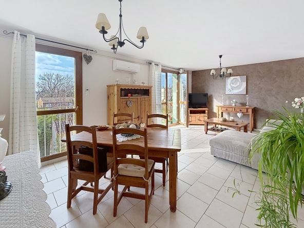 Séjour rectangulaire avec parquet au sol et murs blancs. Baie vitrée coulissante ouvrant sur un balcon avec garde-corps métallique, stores vénitiens aux fenêtres.