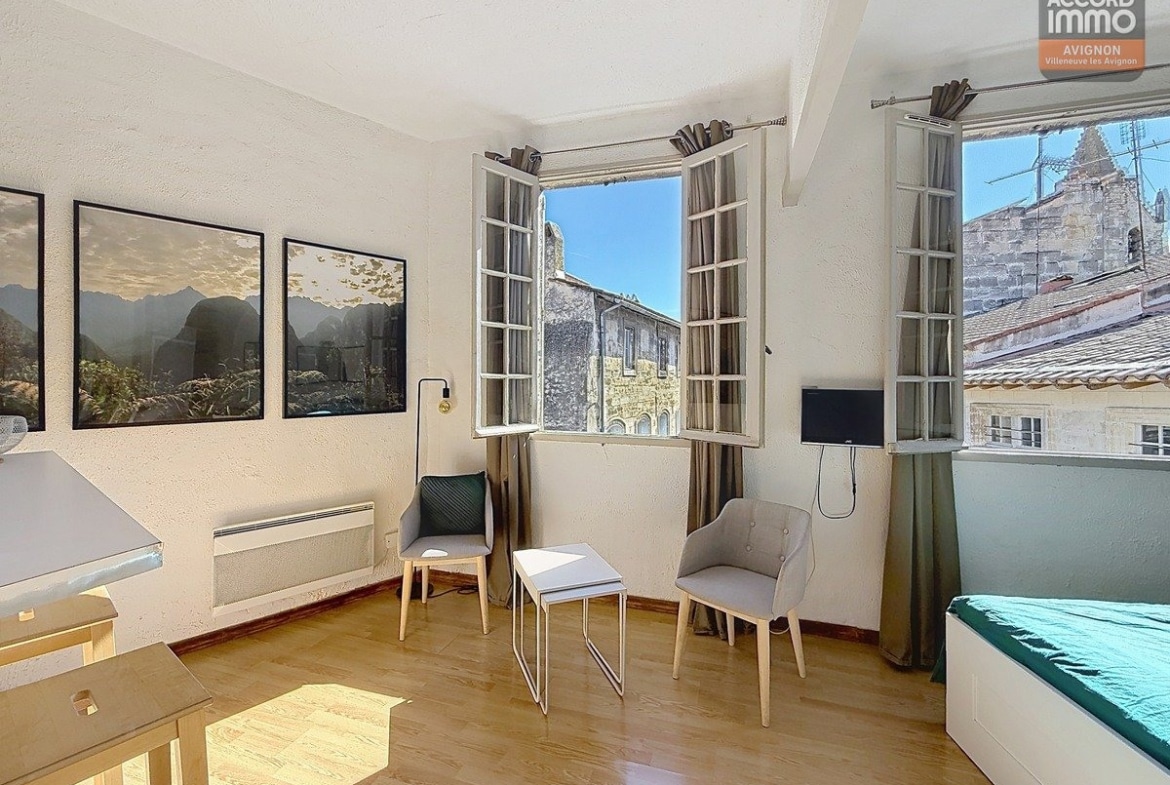 Séjour lumineux avec parquet, double fenêtre vue église, mobilier moderne dans studio dernier étage Avignon