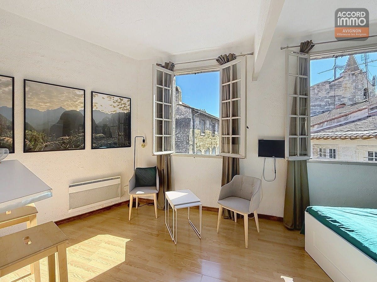 Séjour lumineux avec parquet, double fenêtre vue église, mobilier moderne dans studio dernier étage Avignon