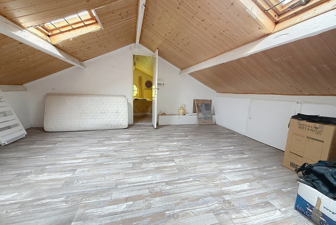 Espace sous combles avec plafond en lambris bois naturel et deux fenêtres de toit. Sol en parquet gris cérusé, pièce de rangement accessible par porte blanche.