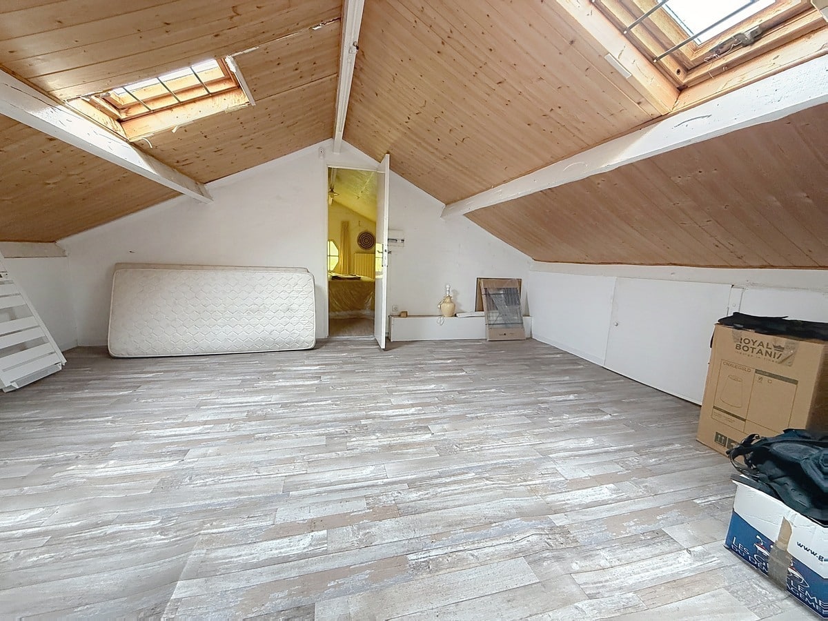 Espace sous combles avec plafond en lambris bois naturel et deux fenêtres de toit. Sol en parquet gris cérusé, pièce de rangement accessible par porte blanche.
