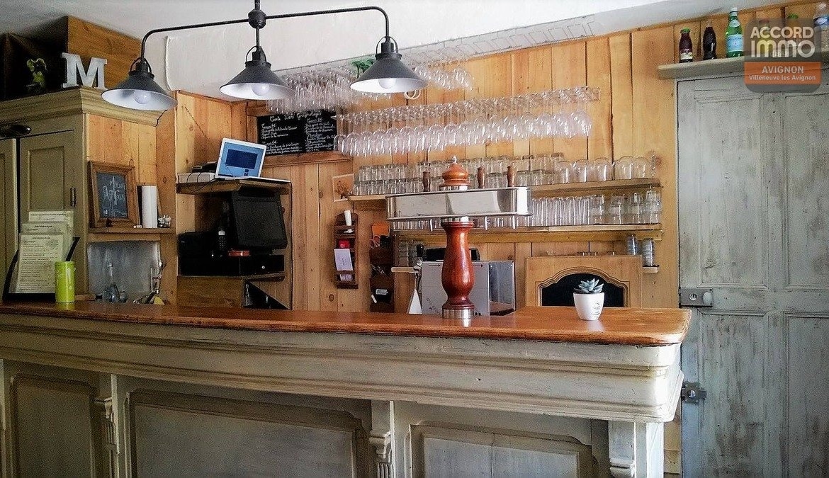 Comptoir de bar patiné blanc avec plateau en bois massif et suspensions industrielles noires. Arrière-bar en pin avec verres suspendus, machine à café professionnelle et caisse enregistreuse.