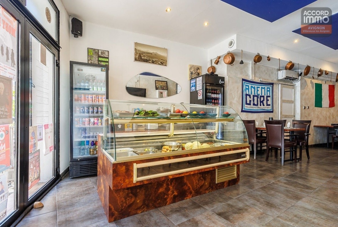 Vitrine réfrigérée avec habillage effet bois verni exposant des ingrédients frais et préparations. Réfrigérateur vertical garni de boissons à gauche, drapeau italien et bannière "Anema e Core" accrochés au mur, casseroles en cuivre suspendues près de la cuisine.