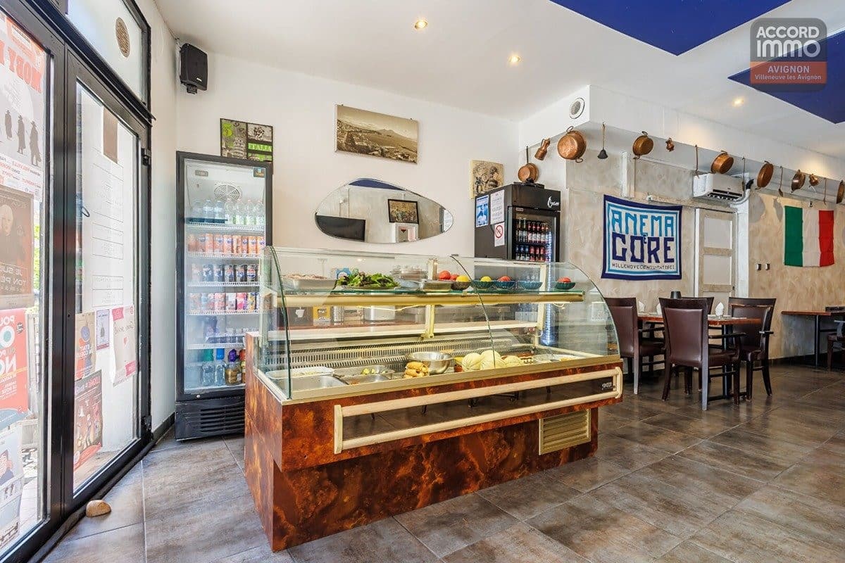 Vitrine réfrigérée avec habillage effet bois verni exposant des ingrédients frais et préparations. Réfrigérateur vertical garni de boissons à gauche, drapeau italien et bannière "Anema e Core" accrochés au mur, casseroles en cuivre suspendues près de la cuisine.