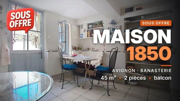 Cuisine carrelée de blanc avec table ronde en verre, deux chaises en fer forgé à assises bleues, fenêtre à battants et étagères murales, maison à vendre à Avignon.