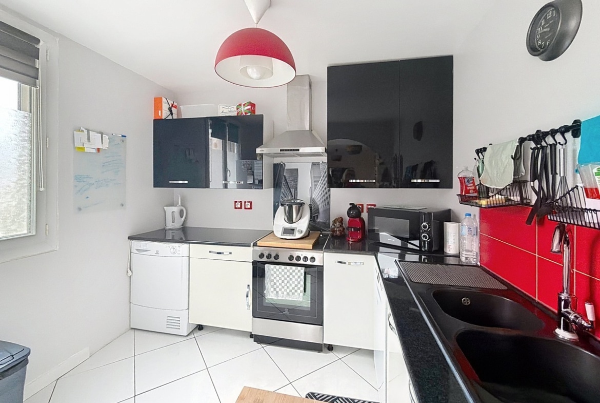 Cuisine ouverte avec meubles intégrés et équipements électroménagers. Plan de travail avec rangements et éclairage fonctionnel au plafond.