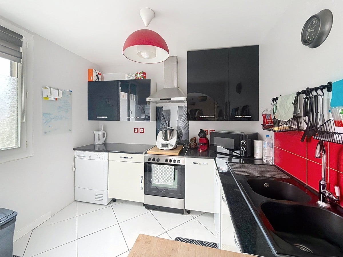 Cuisine ouverte avec meubles intégrés et équipements électroménagers. Plan de travail avec rangements et éclairage fonctionnel au plafond.