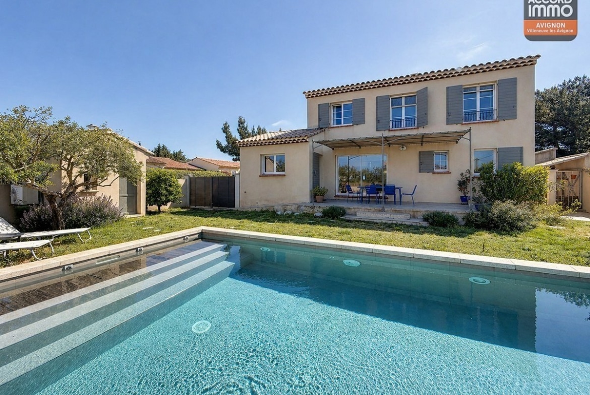 Piscine rectangulaire avec margelles en pierre et eau turquoise au centre d'un jardin engazonné. Terrasse couverte avec pergola en toile et mobilier de jardin bleu devant la maison à étage.