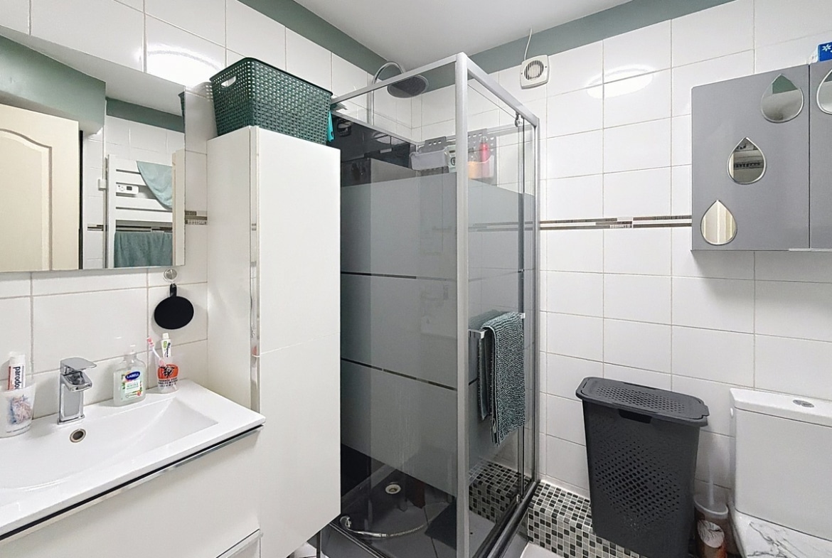 salle d'eau claire avec douche en paroi verre, wc et lavabo et meuble blanc sous lavabo et armoire blanche de rangement