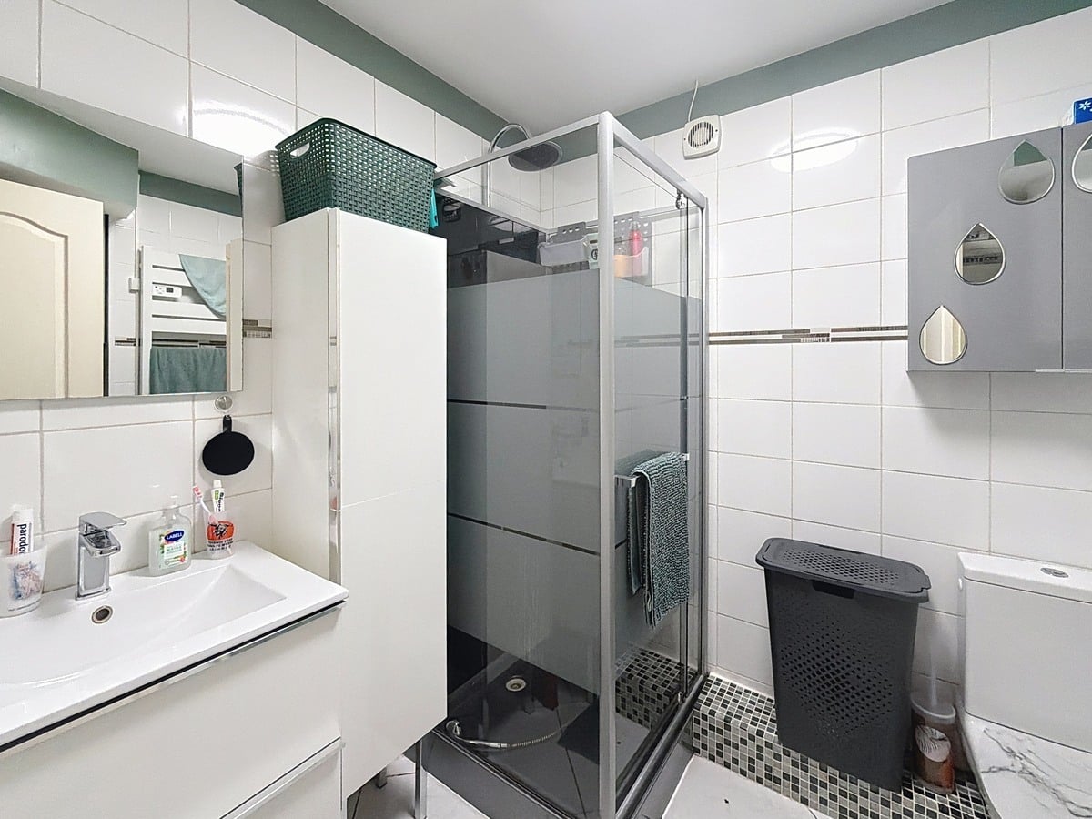 salle d'eau claire avec douche en paroi verre, wc et lavabo et meuble blanc sous lavabo et armoire blanche de rangement