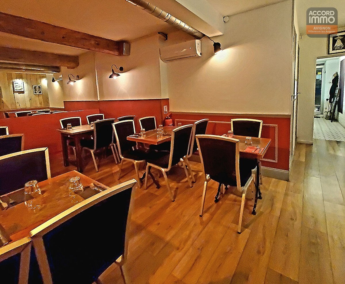 Salle de restaurant avec tables en bois et chaises noires disposées le long d'un mur rouge brique et blanc. Parquet en bois clair, poutres apparentes au plafond, conduit de ventilation métallique et éclairages muraux de style industriel.
