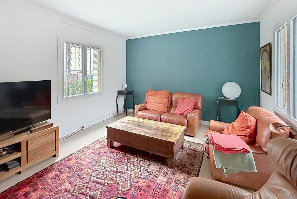 Salon avec trois fauteuils en cuir marron disposés autour d'une table basse en bois massif. Mur d'accent bleu canard, tapis kilim rouge à motifs géométriques et parquet clair.