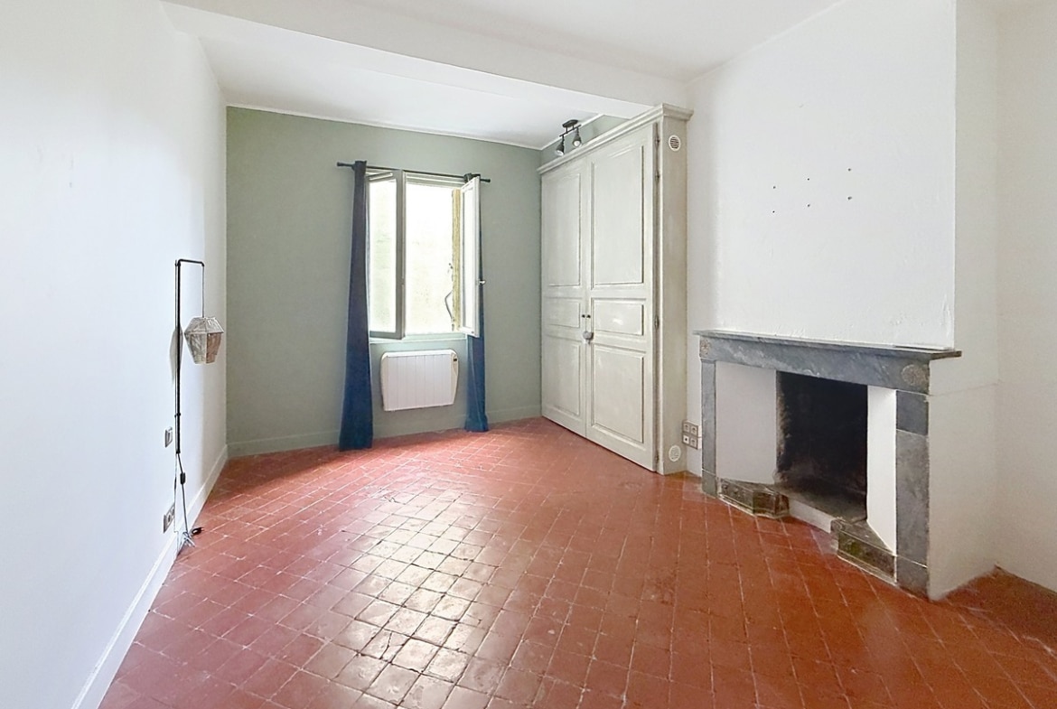 Pièce avec sol en tomettes rouges traditionnelles et cheminée ancienne en marbre gris. Un placard intégré blanc est encastré près de la fenêtre avec rideaux bleu marine, mur d'accent vert sauge.