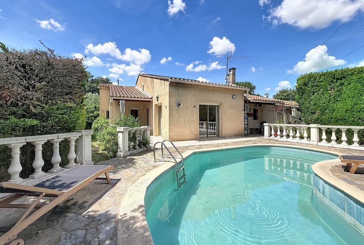Piscine arrondie avec eau turquoise entourée d'une terrasse en pierre et balustrades blanches. Façade de maison provençale enduit ocre avec toiture en tuiles et transats en bois.
